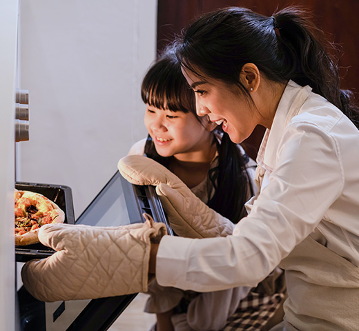 A mother and her daughter take a pizza out of the oven
